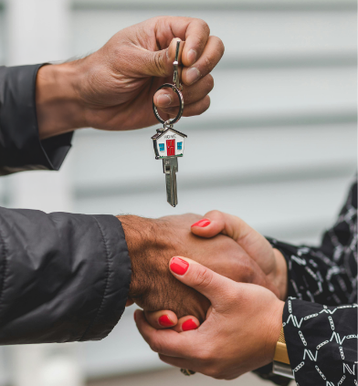 An image of a man shaking a woman's hand and handing her over keys to her new house.